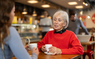 Elderly woman meets her adult daughter in cafe. Conversation over a cup of coffee