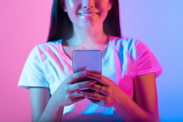 A woman smiles while holding a smartphone, illuminated by vibrant pink and blue lights. The modern...