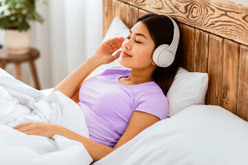 Remote Learning. Chinese Girl In Earphones Listening To Podcast Studying Distantly At Home Lying In...