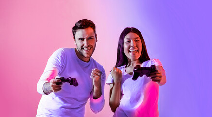 Two friends are joyfully playing video games with controllers in hand. They share smiles and...