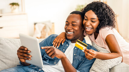 Happily married african american couple buying stuff online from home, using digital tablet and...
