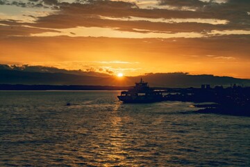 Ferry leaving harbor at golden orange sunset over mountains © Alexander