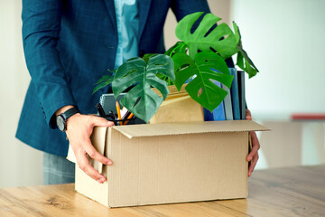 A young Middle Eastern businessman is transporting a box filled with office supplies and potted...