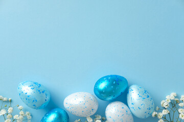Blue and white speckled Easter eggs with white flowers on a pastel blue background. Flat lay, top view.