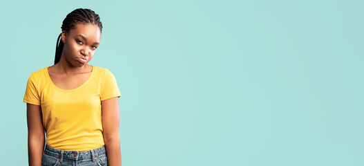 A young woman stands with a frown, showcasing her disappointment. She wears a yellow shirt and...
