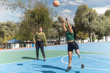 Young latin american woman with prosthetic leg playing basketball with friend outdoors
