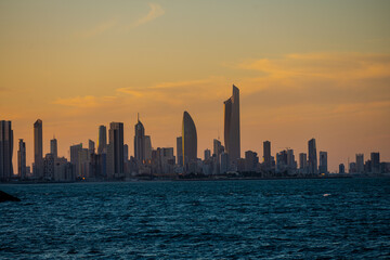 Naklejka premium Kuwait City Skyline at Dusk with Al Hamra Tower and Modern Skyscrapers Reflecting the Warm Sunset Over the Arabian Gulf