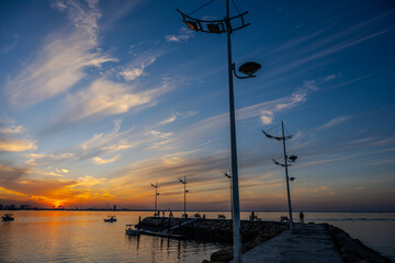 Scenic Sunset at a Kuwait Fishing Pier with Boats, Streetlights, and a Dramatic Sky Over the...