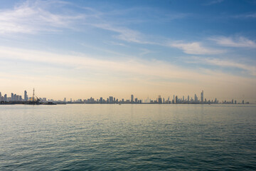 Naklejka premium Panoramic View of Kuwait City Skyline with Calm Arabian Gulf Waters and Marina Waves at Sunrise