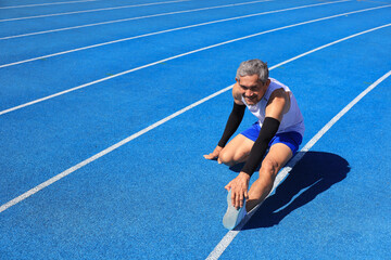 Senior Asian athlete doing stretching warm up for running in the professional blue track for...