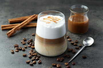 Tasty latte macchiato in glass, coffee beans and cinnamon on grey table, closeup