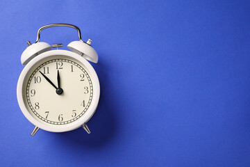 One white alarm clock on blue background, top view. Space for text