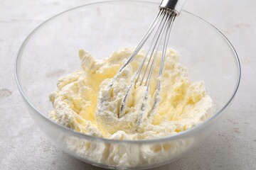 Whisking whipped cream in bowl on light grey table, closeup
