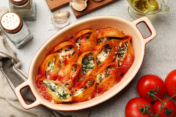 Delicious conchiglie pasta with ricotta cheese, spinach and tomato sauce in baking dish on gray...