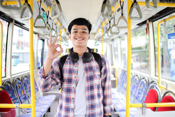 Positive Asian Male In Casual Style Looking At Camera And Showing Okay Sign While Standing On Bus