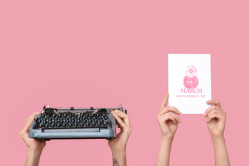 Hands holding vintage typewriter and festive postcard with text 8 MARCH HAPPY WOMEN'S DAY on pink...