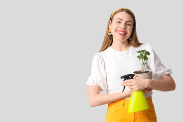 Beautiful young woman with water sprayer and houseplant on grey background