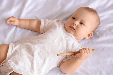 Cute little baby with rattle lying on bed in room at home