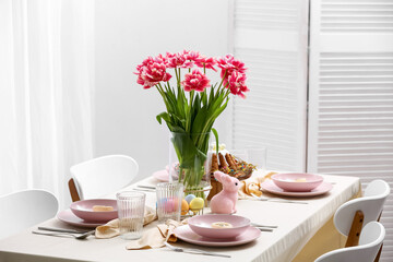 Table setting with Easter cake, painted eggs and flowers in room