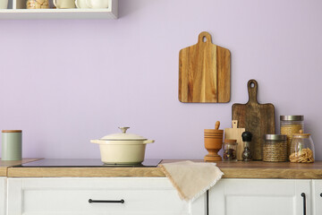 Stove with cooking pot and utensils on counters near lilac wall in kitchen