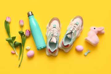 Composition with stylish sneakers, bottle of water, Easter decor and tulip flowers on yellow...