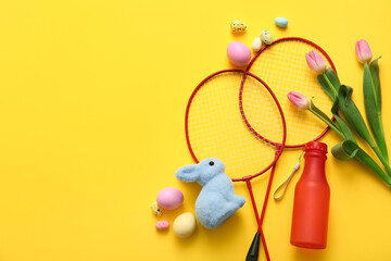 Composition with badminton rackets, bottle of water, Easter eggs and tulip flowers on yellow...