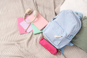 Backpack with books, pencil case and headphones on bed, top view