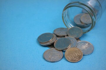 Coins spilling from a glass bottle on a blue background. Financial concept.