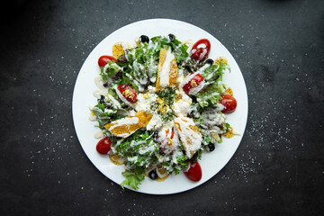 Fresh and colorful salad with tomatoes, olives and orange slices on a white plate.