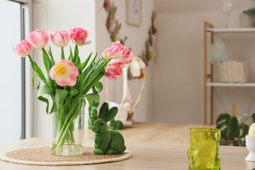 Vase with tulips and Easter rabbit on table in kitchen, closeup