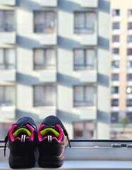 Pair of sneakers drying on the windowsill after playing sports. View from window to building facades. Active lifestyle desire concept. Vertical photo.