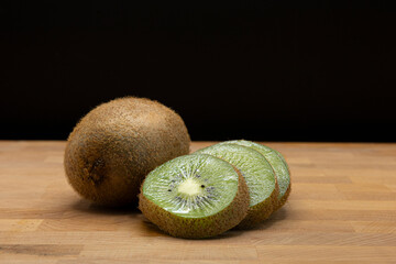 Fresh kiwi fruit rests on a rustic butcher's block cutting board, showcasing the vibrant green...