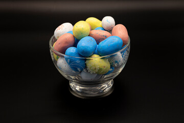 A glass bowl filled with colorful Easter candy, featuring pastel chocolate eggs, jelly beans, and sugary treats. A festive and vibrant display perfect for celebrating the spring holiday.