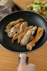 An exquisite dish featuring perfectly fried golden chicken pieces, delicately sizzling in a pan, accompanied by a refreshing, vibrant tomato salad. The rustic kitchen setting enhances the authentic ch