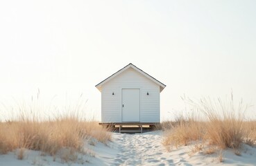 Solitary white beach cabin standing on stilts on sandy coast. Grass clumps around. Calm tranquil mood, idyllic coastal architecture. Summer vacation background, travel destination concept, minimal