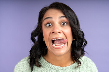 Woman sticking out tongue and making funny face on purple background