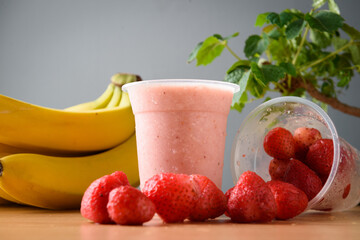 Strawberry and banana smoothie in plastic glass on wooden table
