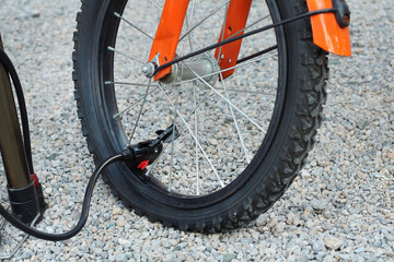 Close up of hand bicycle pump inflating flat tire bike on dirt road with selective focus.
