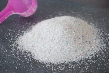 White laundry detergent powder with a pink scoop on a dark surface