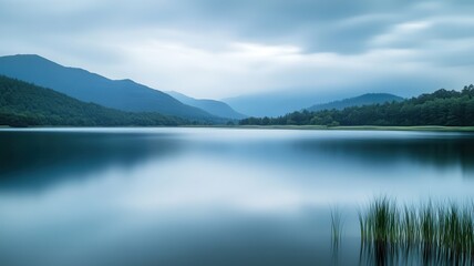 Naklejka premium Calm lake, misty mountains, serene dawn