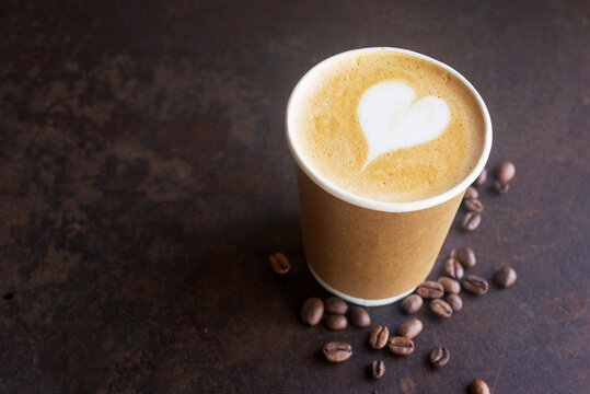 hot latte coffee in takeaway paper coffee cup, ready to go coffee on brow rustic table.