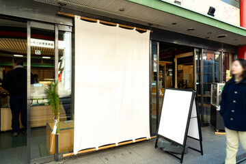 White curtain hanging in entrance of restaurant with glass doors, blank signboard outside, street...