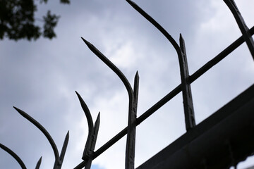Wrought iron fence with pointed finials, silhouetted against a cloudy sky