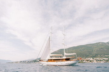 Obraz premium Luxury sailing yacht sails on the sea against the backdrop of green mountains