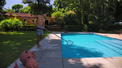 A Man is Using a Pool Leaf Skimmer to Clean the Swimming Pool - Static Shot - Powered by Adobe