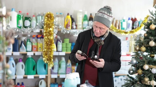 In X mas, senior man sniffs fragrance of perfume, choose scent spray with pleasant smell. Customer pulverize perfume, chooses toilet water. Client sprays perfume, snuff it and chooses perfume