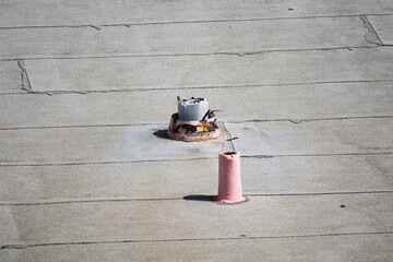 Two cylindrical roof vents, one partially damaged with exposed wires, protrude from a flat weathered rooftop with visible tar seams