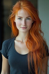 Fototapeta premium A young woman with lively copper-red wavy hair, minimal makeup, and a black top stands in front of a neutral background, showcasing professional hair color and styling