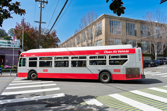 SF Muni Clean Air Vehicle bus navigates a city street intersection, surrounded by urban architecture, crosswalk markings, and greenery - San Francisco, California, USA - March 15, 2025