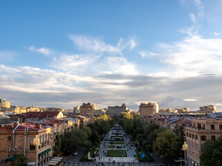 Fototapeta premium Scene of Yerevan cityscape with street buildings and trees, sunlight on sunset on blue sky background, high view from Yerevan cascade, a modern architecture building complex at Yerevan, Armenia.